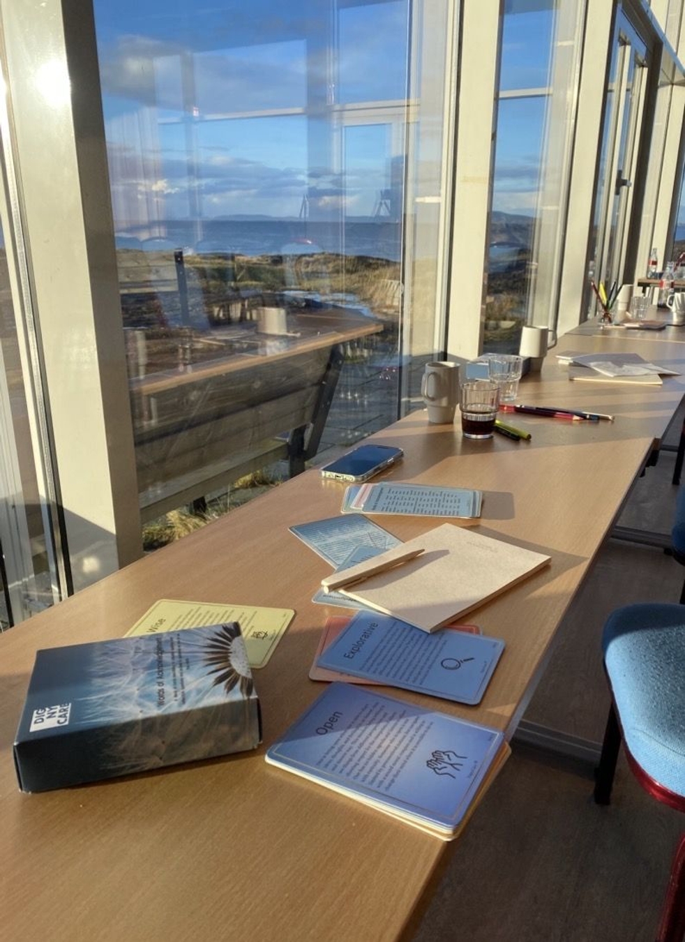 [Visible text on cards and materials on the desk]
Explore
Open
Reflect
[Book title partially visible]
Dee...