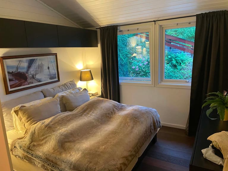A cozy bedroom interior featuring a nautical theme with warm, inviting ambiance. The room showcases a comfortable bed dressed in luxurious cream and beige