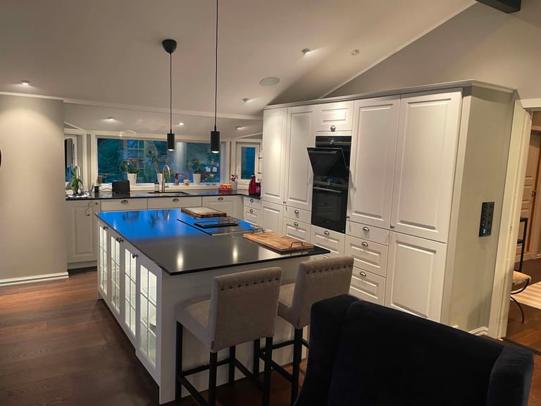 A modern, elegant kitchen featuring a sophisticated design with white shaker-style cabinetry and a striking central island with dark countertops. The space