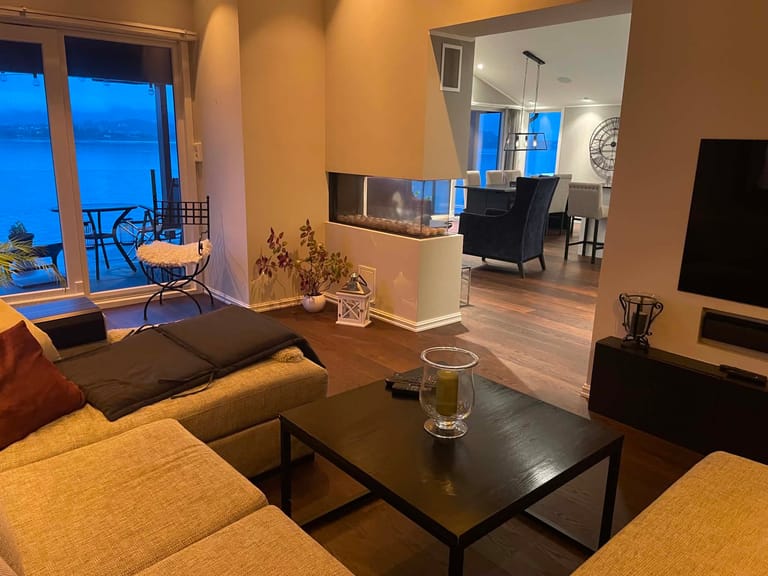 A modern, cozy living space featuring an open-concept design with warm ambient lighting during evening hours. The room showcases a contemporary interior with a