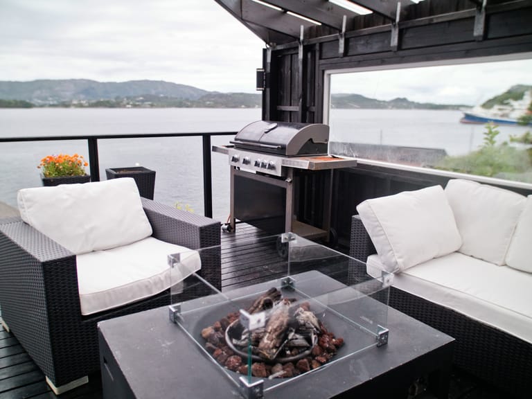 A luxurious waterfront patio or deck setup featuring modern outdoor living and entertainment space. The scene showcases a contemporary outdoor lounge area with